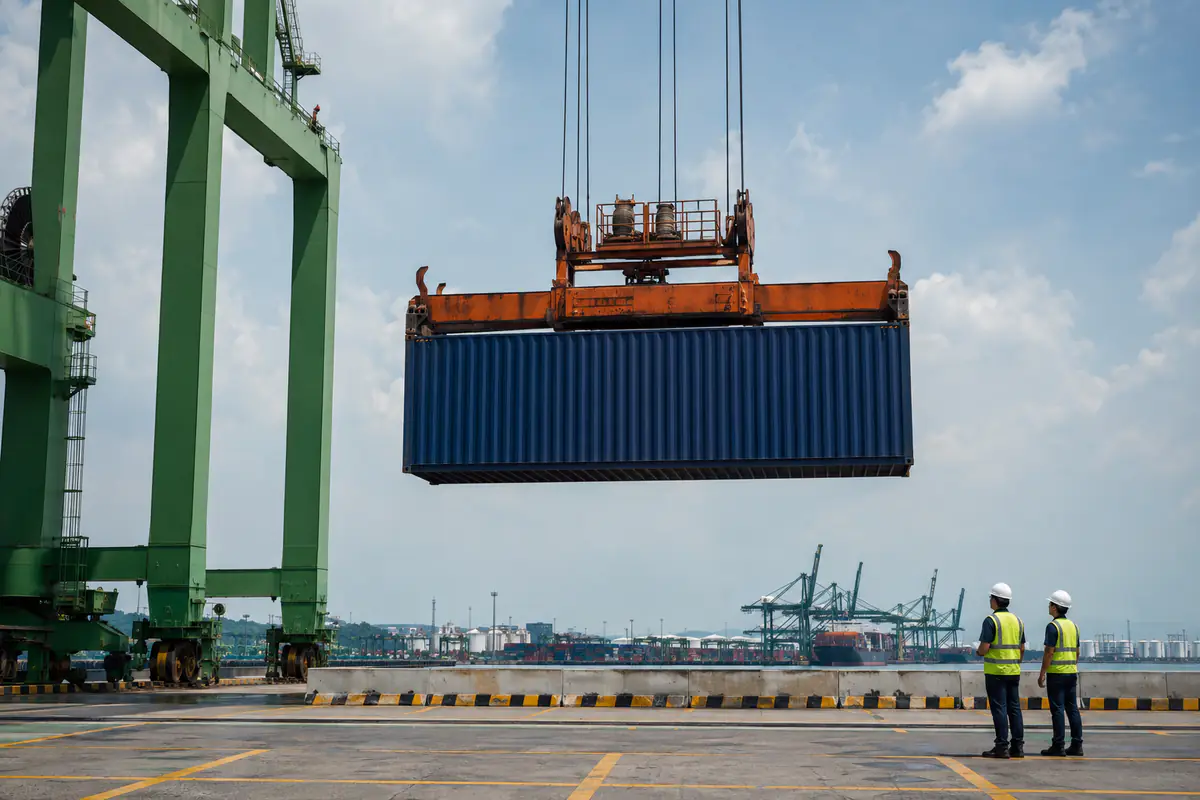 Kren mengangkat kontena tanpa jenama dengan pekerja di luar zon angkat